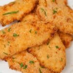 A plate of crispy and juicy air fryer chicken tenders stacked on top of each other.