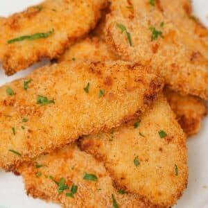 A plate of crispy and juicy air fryer chicken tenders stacked on top of each other.