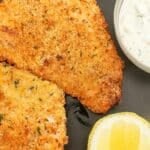 Crispy air fryer fish fillets on a plate with tartar sauce and a lemon wedge.