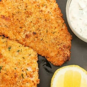 Crispy air fryer fish fillets on a plate with tartar sauce and a lemon wedge.