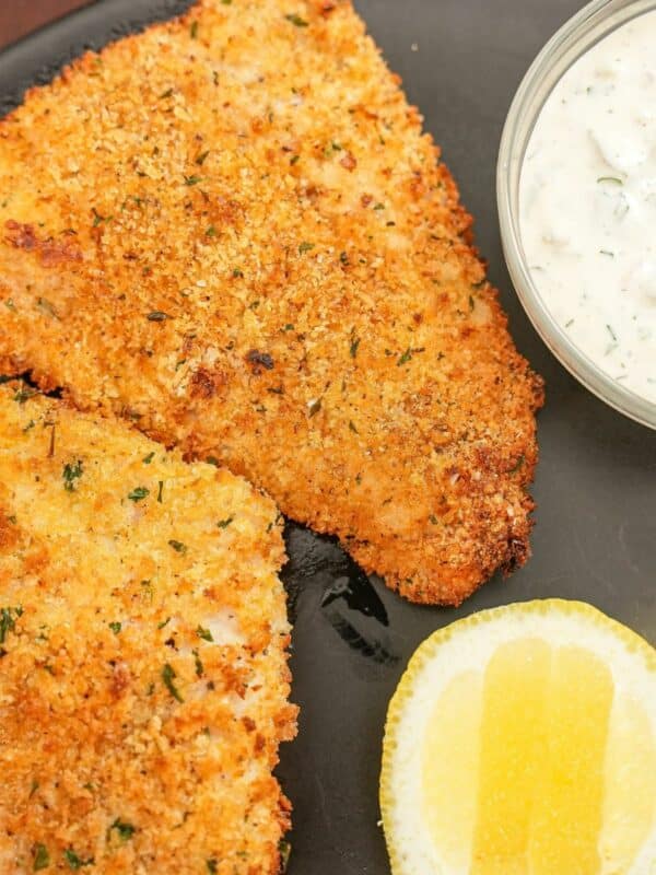 Crispy air fryer fish fillets on a plate with tartar sauce and a lemon wedge.