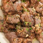 Cooked air fryer steak bites in a bowl tossed in an herb garlic butter.