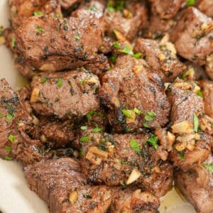 Cooked air fryer steak bites in a bowl tossed in an herb garlic butter.