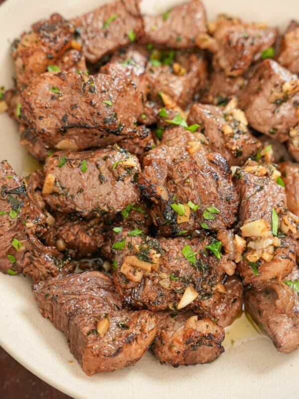 Cooked air fryer steak bites in a bowl tossed in an herb garlic butter.