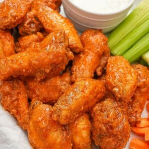 Fried buffalo wings on a parchment paper lined tray with ranch dressing, celery, and carrots.