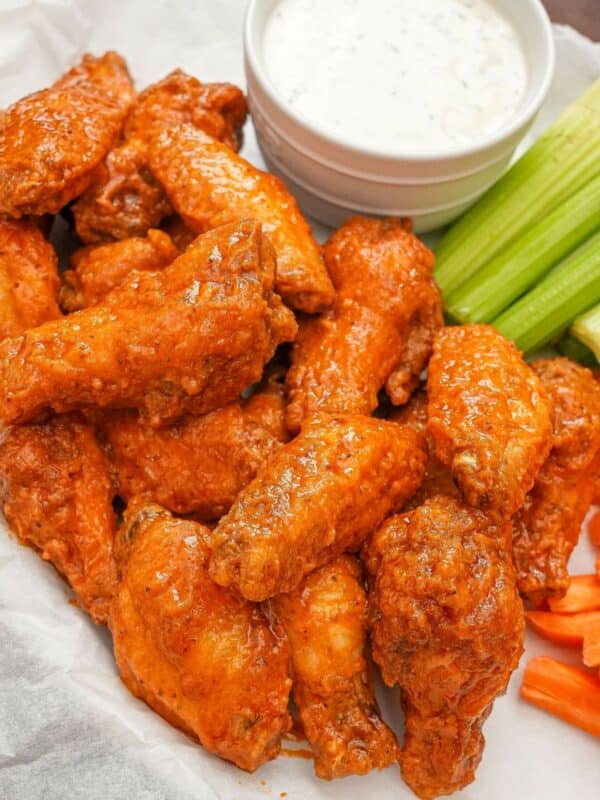 Fried buffalo wings on a parchment paper lined tray with ranch dressing, celery, and carrots.