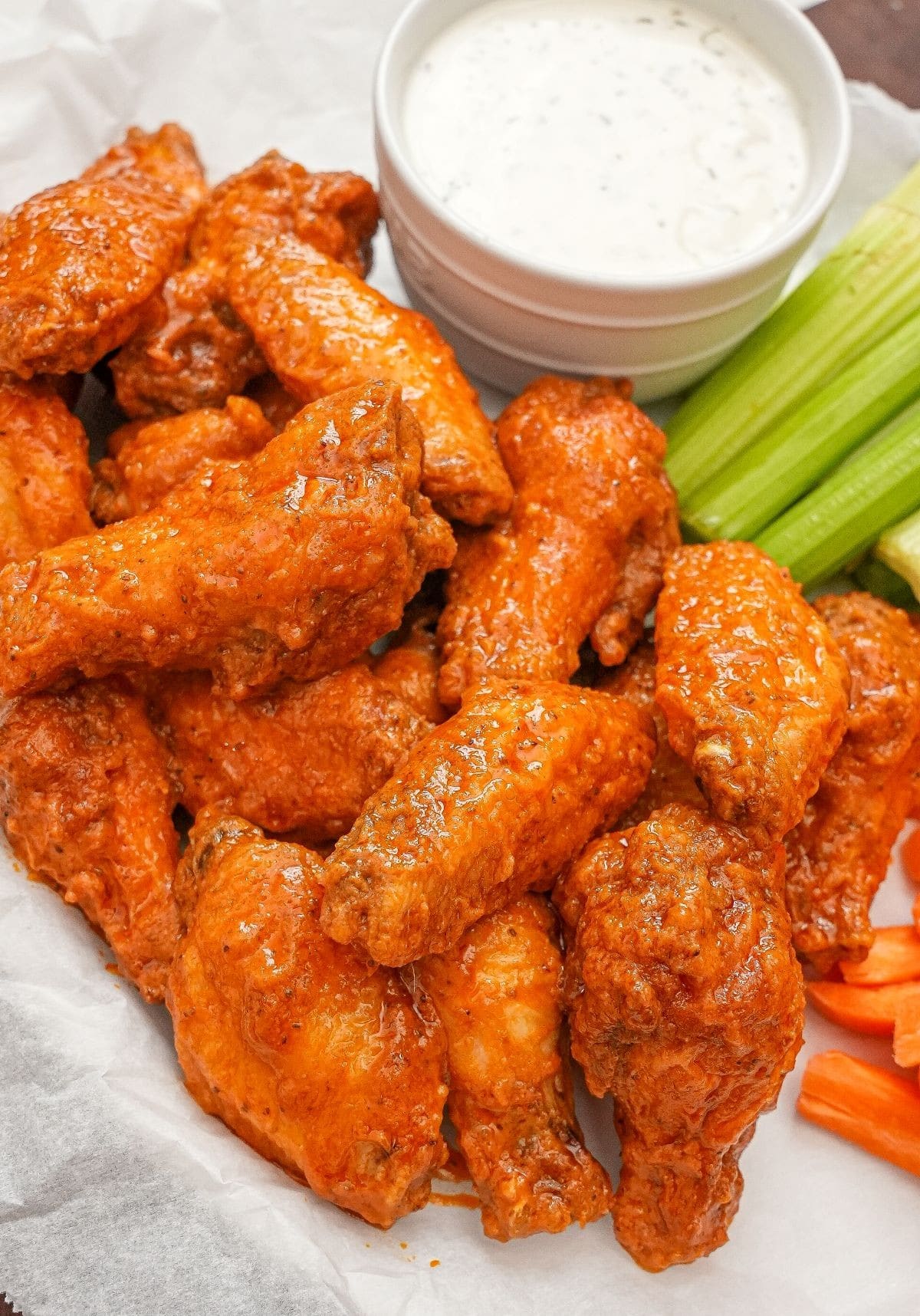 Fried buffalo wings on a parchment paper lined tray with ranch dressing, celery, and carrots.