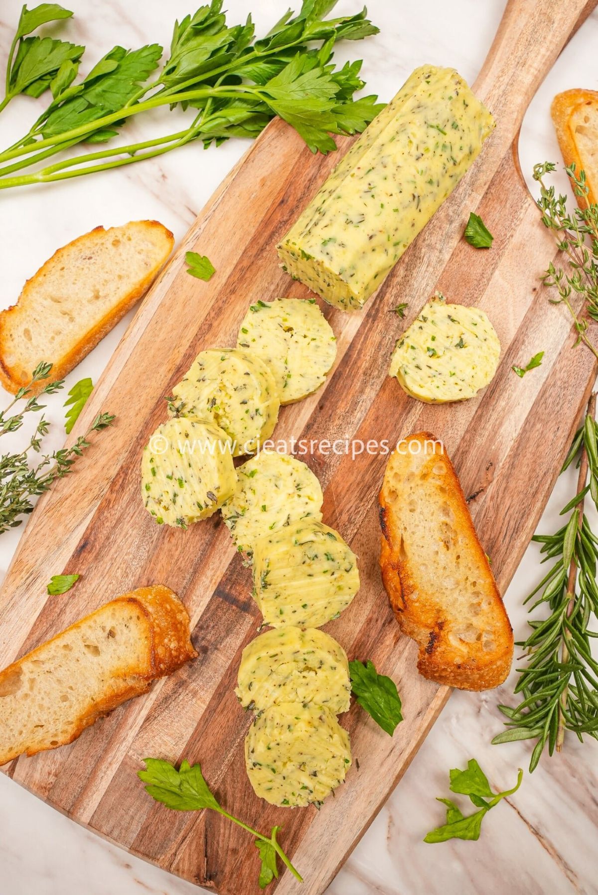 Garlic herb compound butter on a cutting board with herbs and bread. The butter is cut into circles.