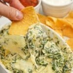 A chip scooping Houstons Copycat Spinach Artichoke dip with chips.