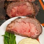 Sliced Prime Rib on a plate with mashed potatoes and green beans.