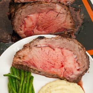 Sliced Prime Rib on a plate with mashed potatoes and green beans.