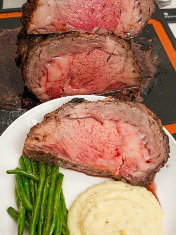 Sliced Prime Rib on a plate with mashed potatoes and green beans.