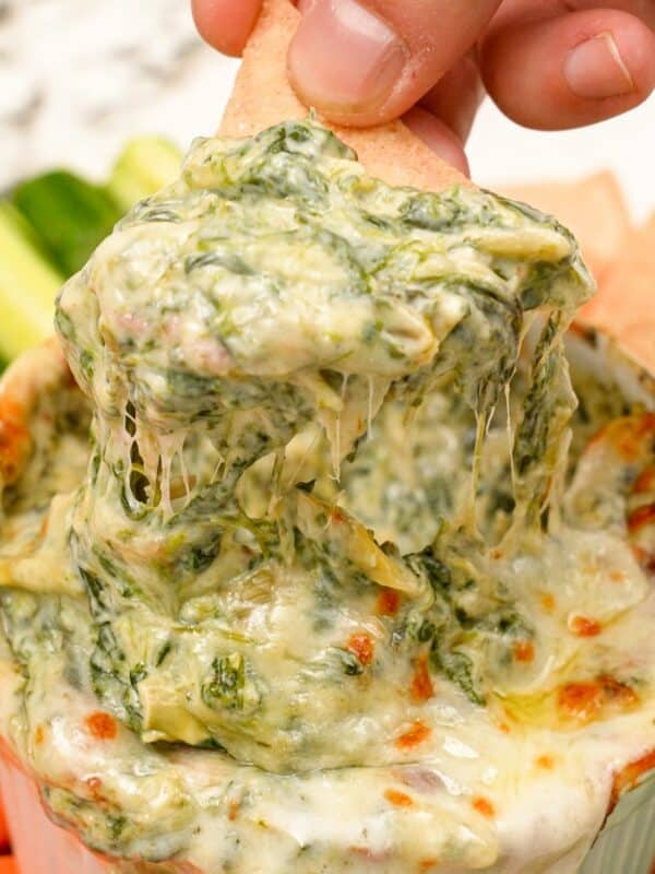 A hand scooping spinach artichoke dip with a tortilla chip.