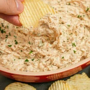 A hand scooping Caramelized Onion Dip with thick cut potato chips.