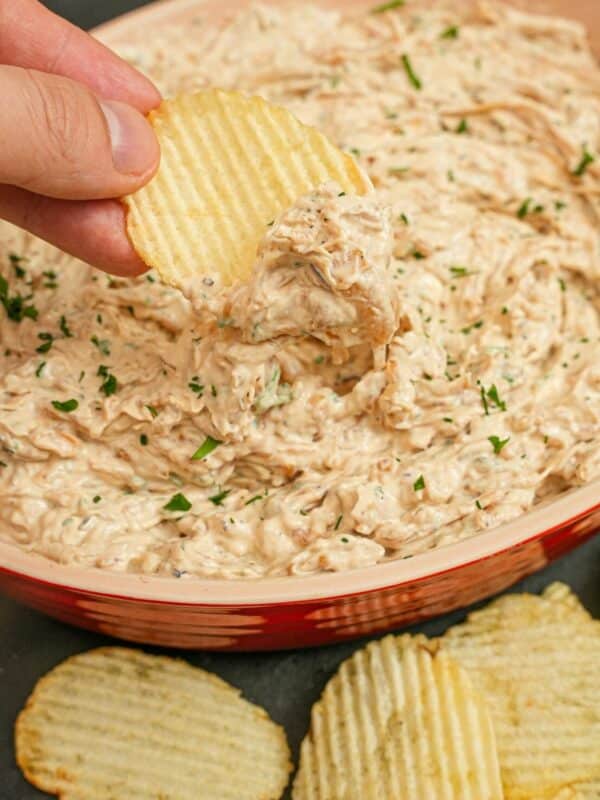 A hand scooping Caramelized Onion Dip with thick cut potato chips.