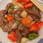 A photo of Chinese Pepper Steak over a bed of white rice in a grey circular bowl.