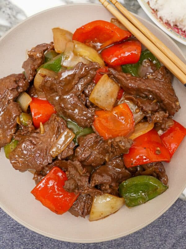 A photo of Chinese Pepper Steak over a bed of white rice in a grey circular bowl.
