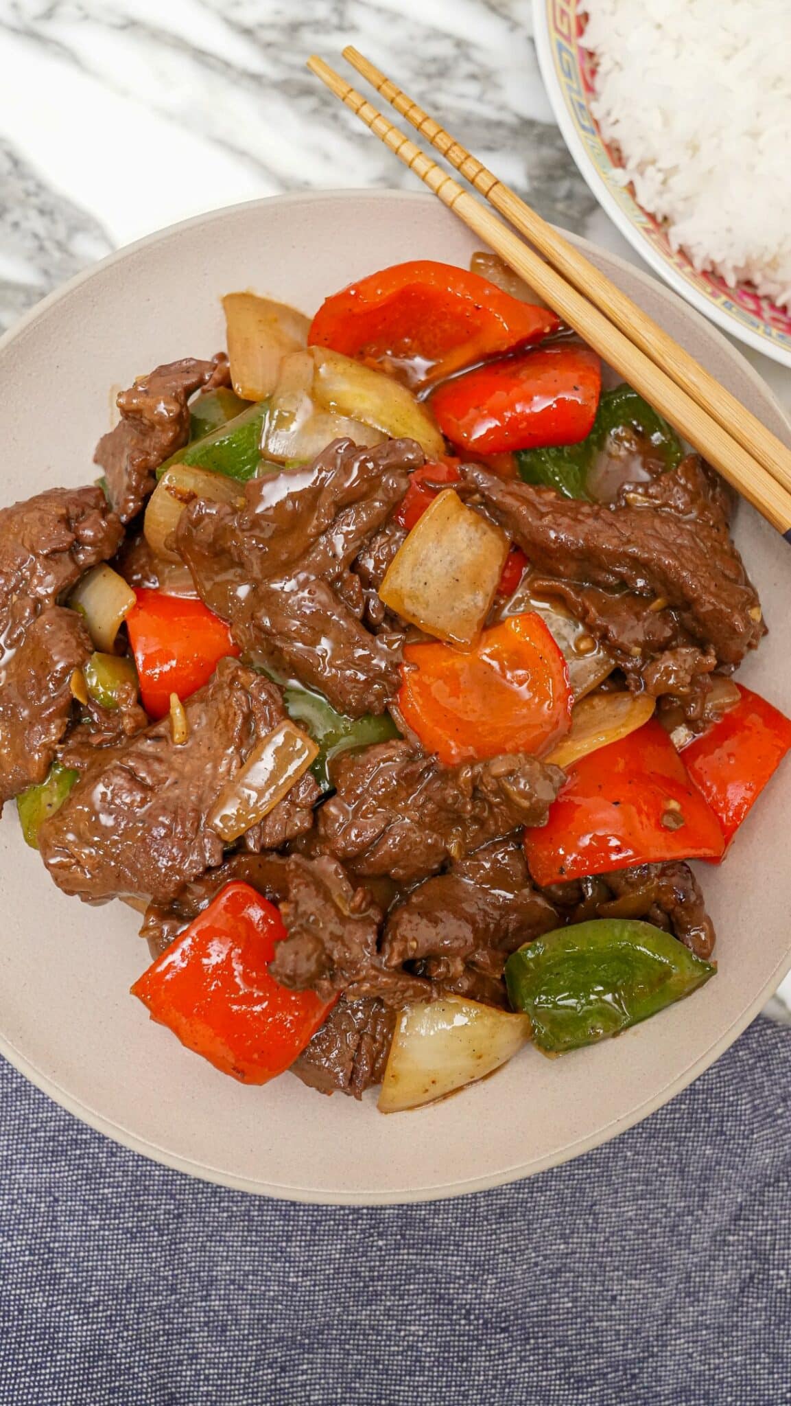 A photo of Chinese Pepper Steak over a bed of white rice in a grey circular bowl.