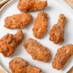 A plate of crispy fried chicken wings next to a baking sheet of freshly fried wings.