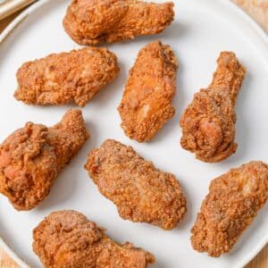 A plate of crispy fried chicken wings next to a baking sheet of freshly fried wings.