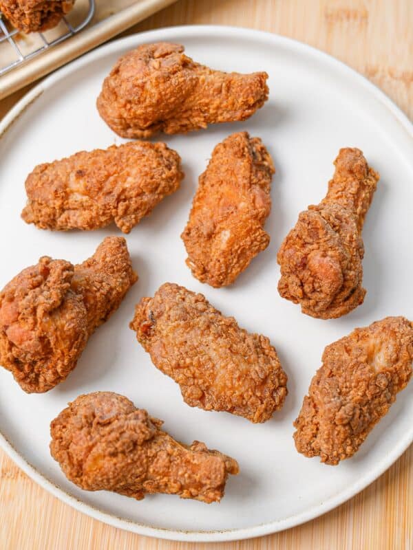 A plate of crispy fried chicken wings next to a baking sheet of freshly fried wings.
