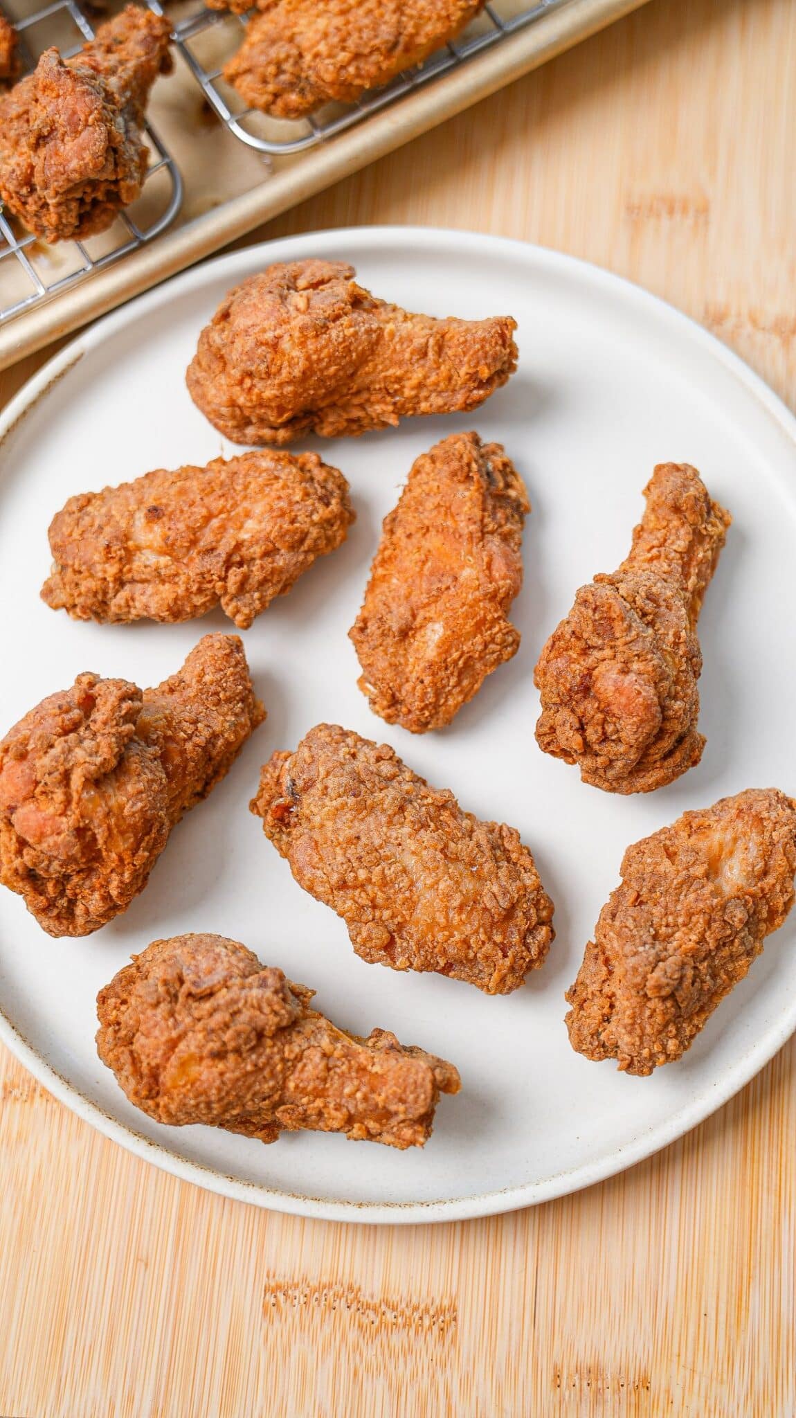 A plate of crispy fried chicken wings next to a baking sheet of freshly fried wings.